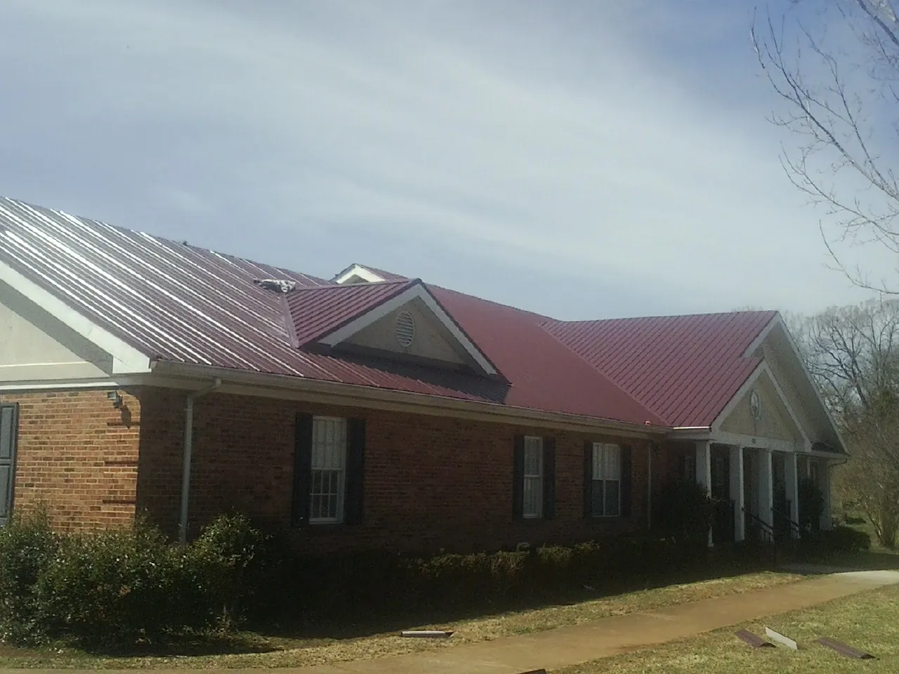 Red metal roof with gabled entries on a long brick building, from a Hail Damage Roof Repair job in Big Stone Gap