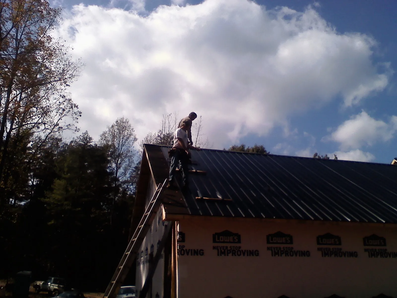 Roofer fastening dark metal panels high against a cloudy sky, from a Roof Inspection job in Big Stone Gap