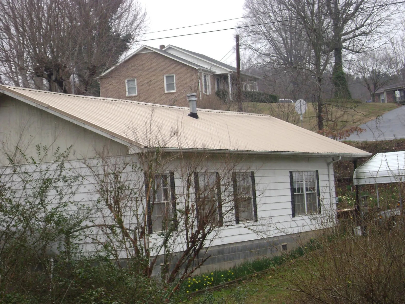 Tan metal roof on a white sided house set into a hillside — Commercial Roofing by Roofing Brothers in Big Stone Gap